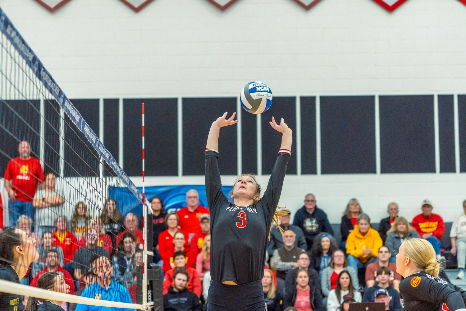 Volleyball players and spectators in red uniforms react excitedly during an intense match at an indoor sports venue.