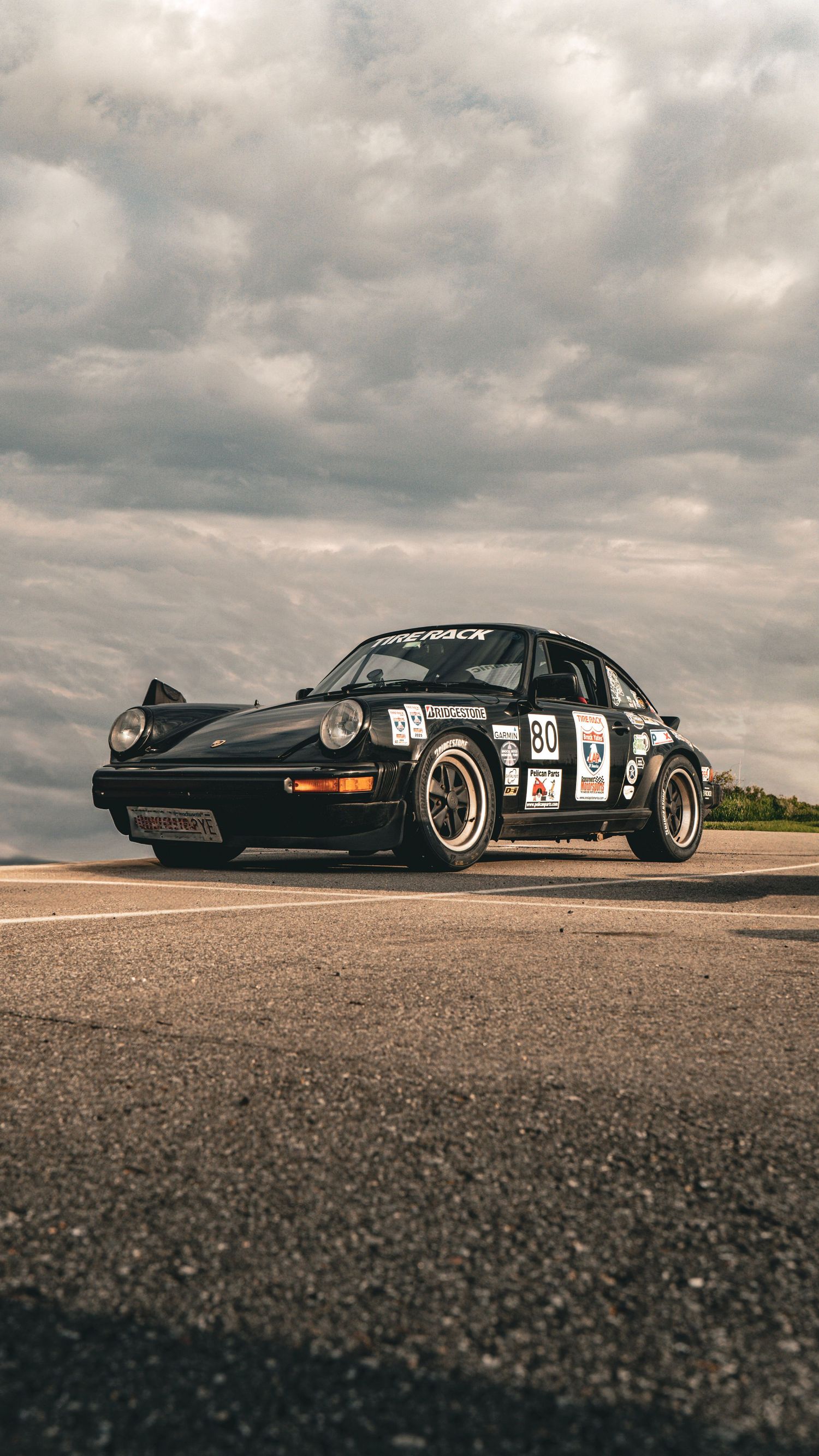 Black vintage racing cars lined up on a track under dramatic cloudy skies.