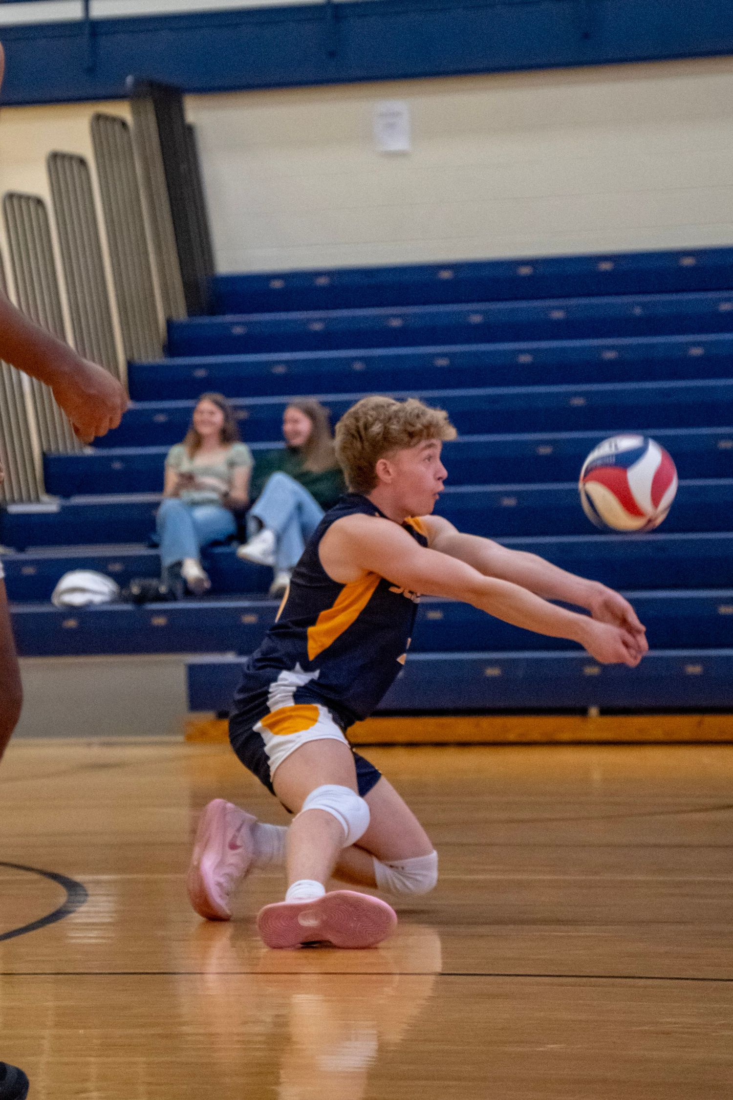 Player in navy and gold uniform dives to bump volleyball during indoor match.
