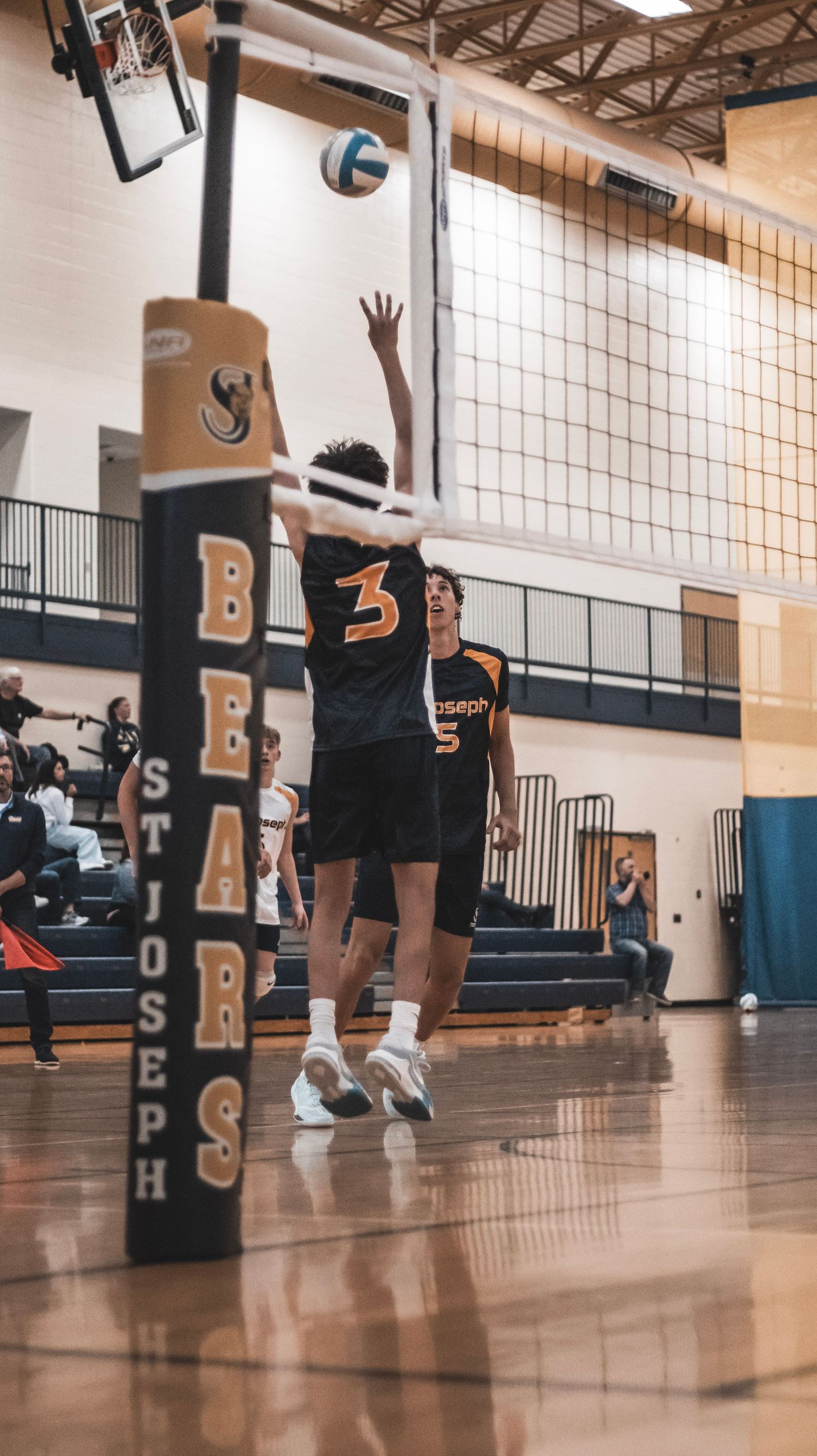 A player in a black jersey jumps to block at the volleyball net.