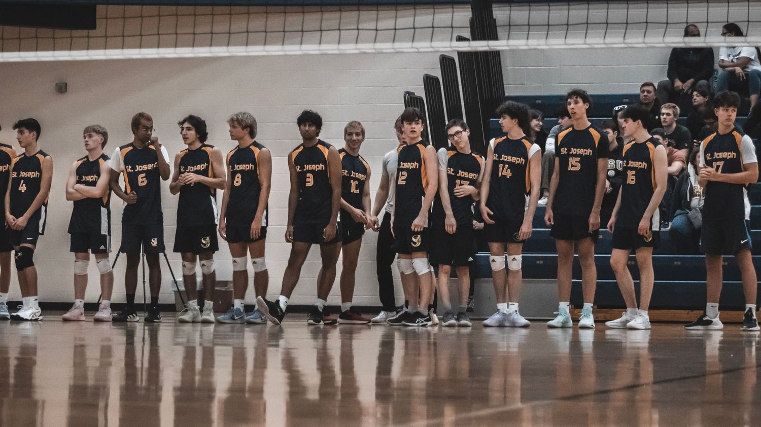 Team in black uniforms lines up along sideline during volleyball match.