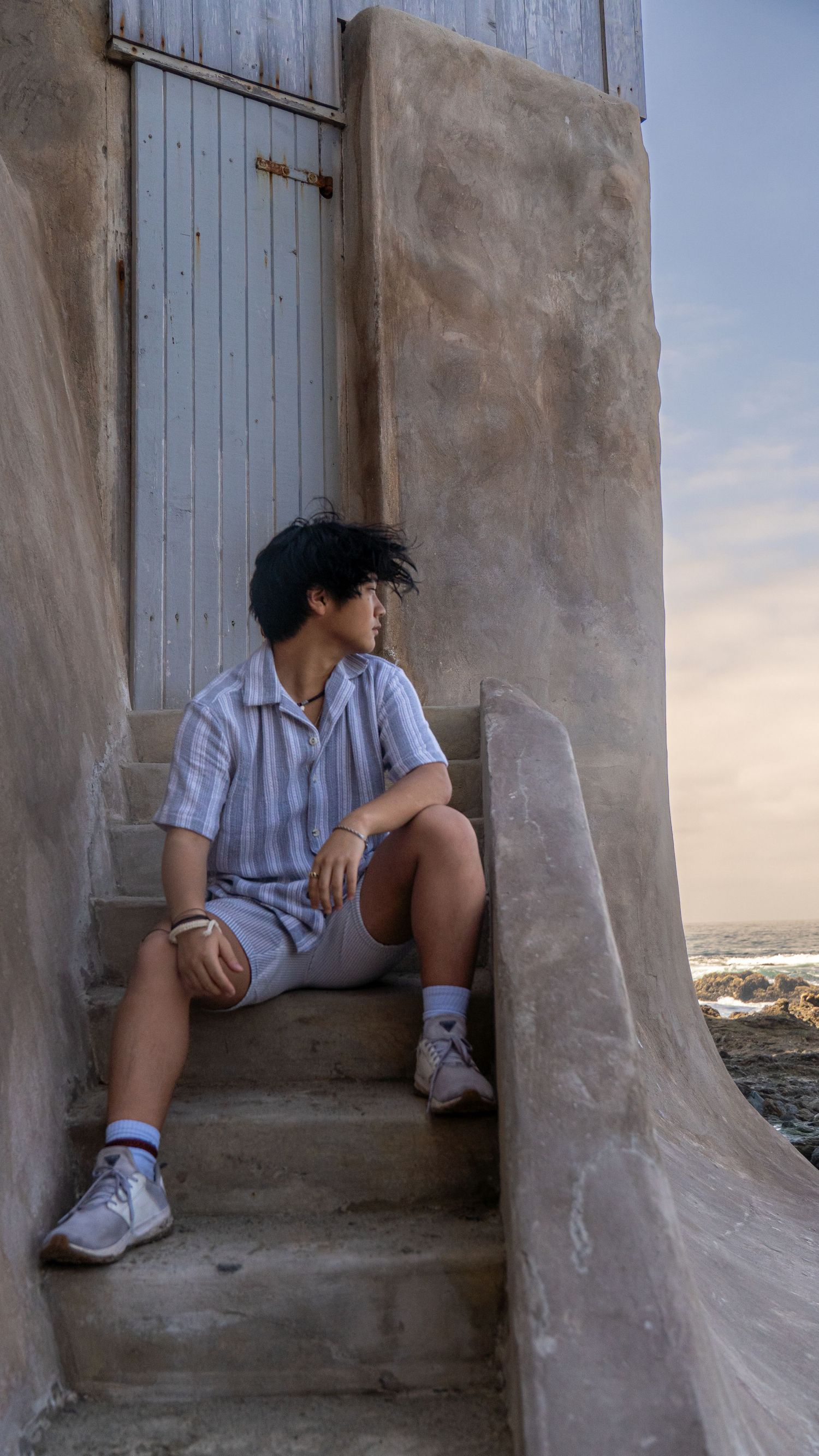 Person in striped shirt sitting on stone steps at sunset.