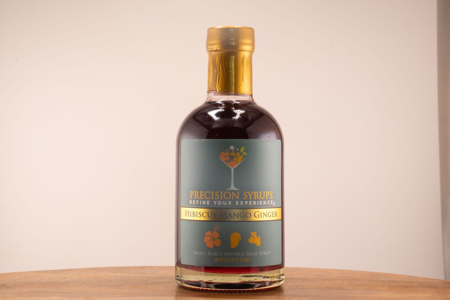 Gold-capped dark spirits bottle with tree emblem and gray label on wooden table.