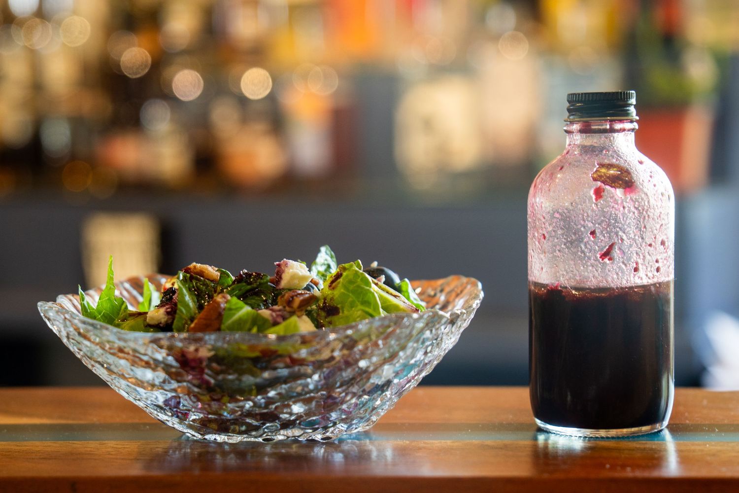 Bar ingredients including salad, syrup, and cocktail components arranged on a wooden surface.