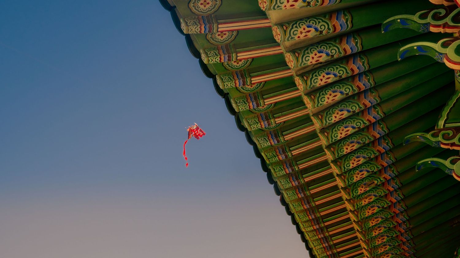 Angular view of Korean temple eaves with decorative paintwork against blue sky.