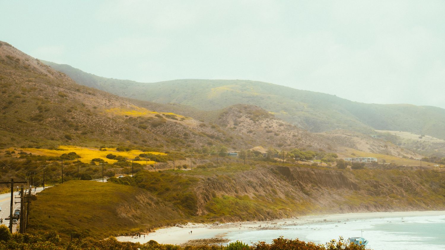 Dramatic coastal landscape with rolling hills and sandy beach along misty shoreline.