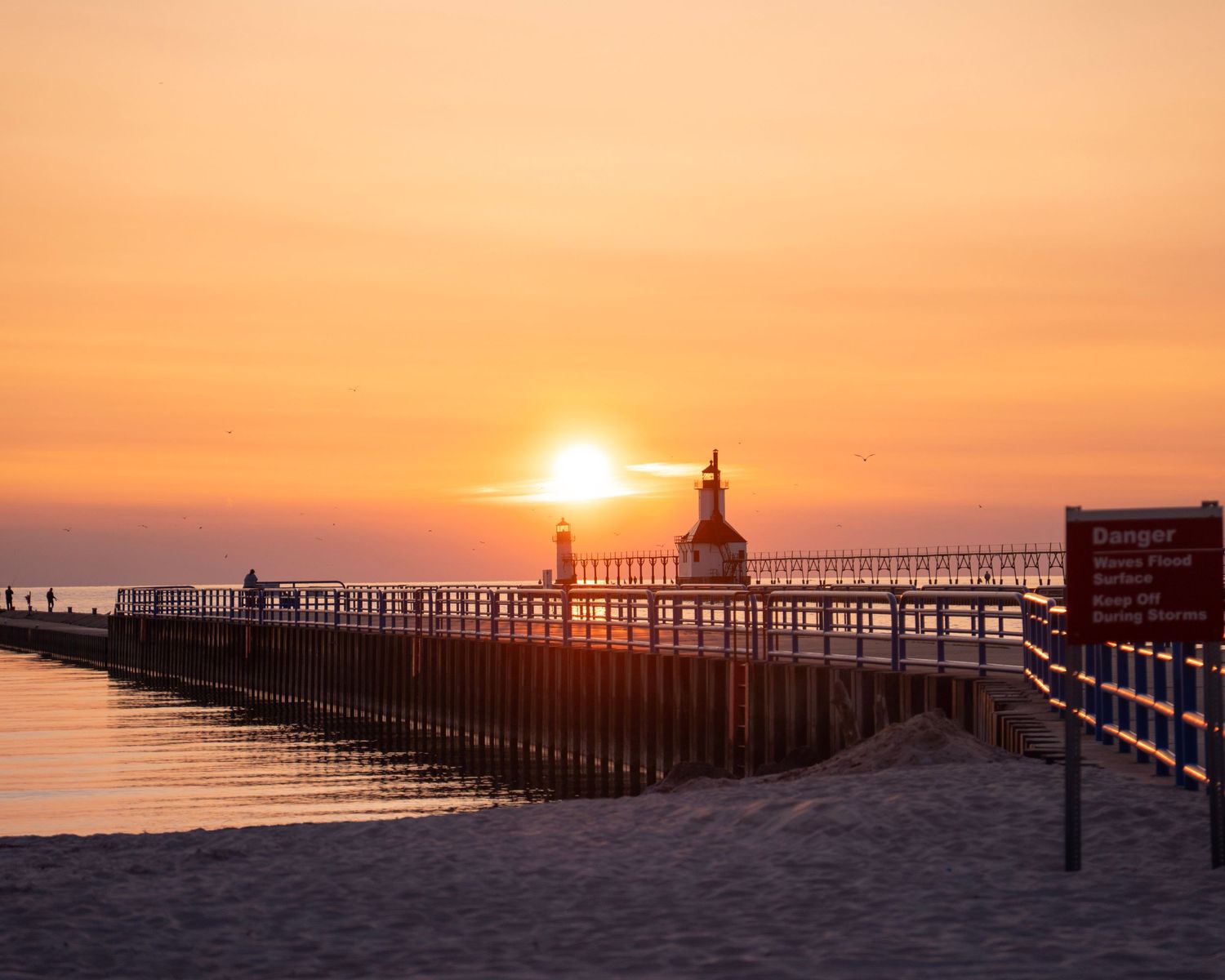 Historic lighthouse on pier at sunset with golden light reflecting on calm waters.