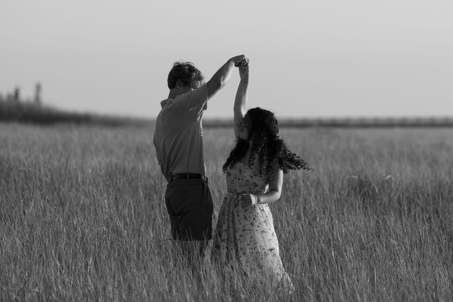 Couple shares a romantic dance in tall grass field at sunset creating a silhouetted black and white moment.