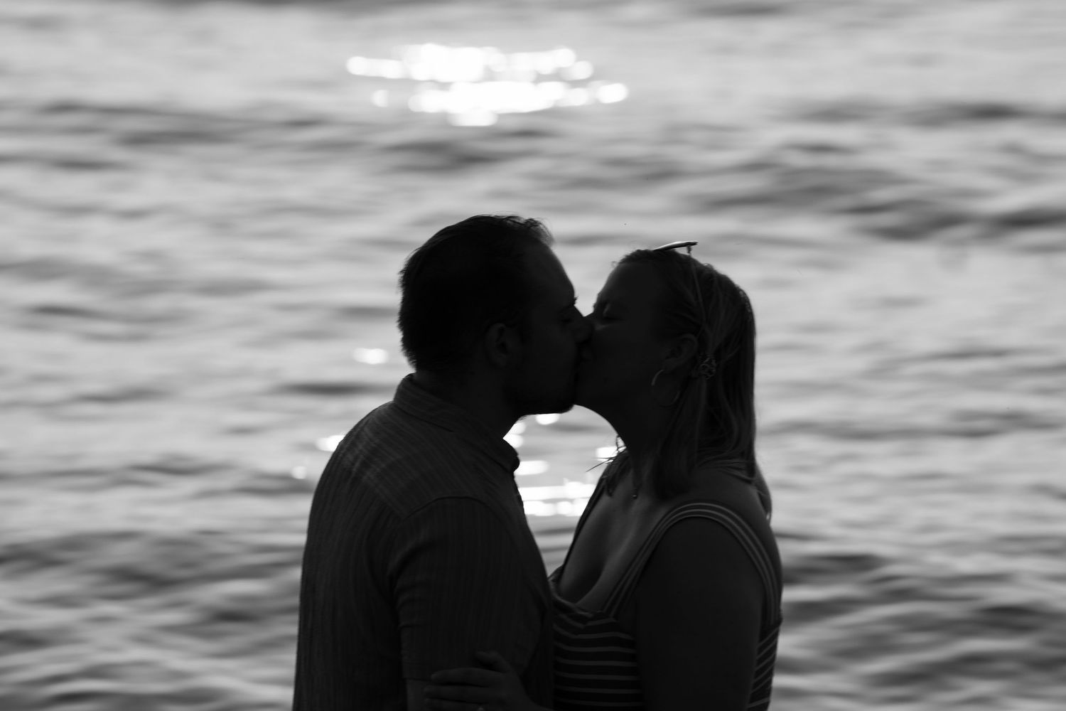 A romantic silhouetted figures sharing a kiss at sunset on the beach against a rippling ocean backdrop.