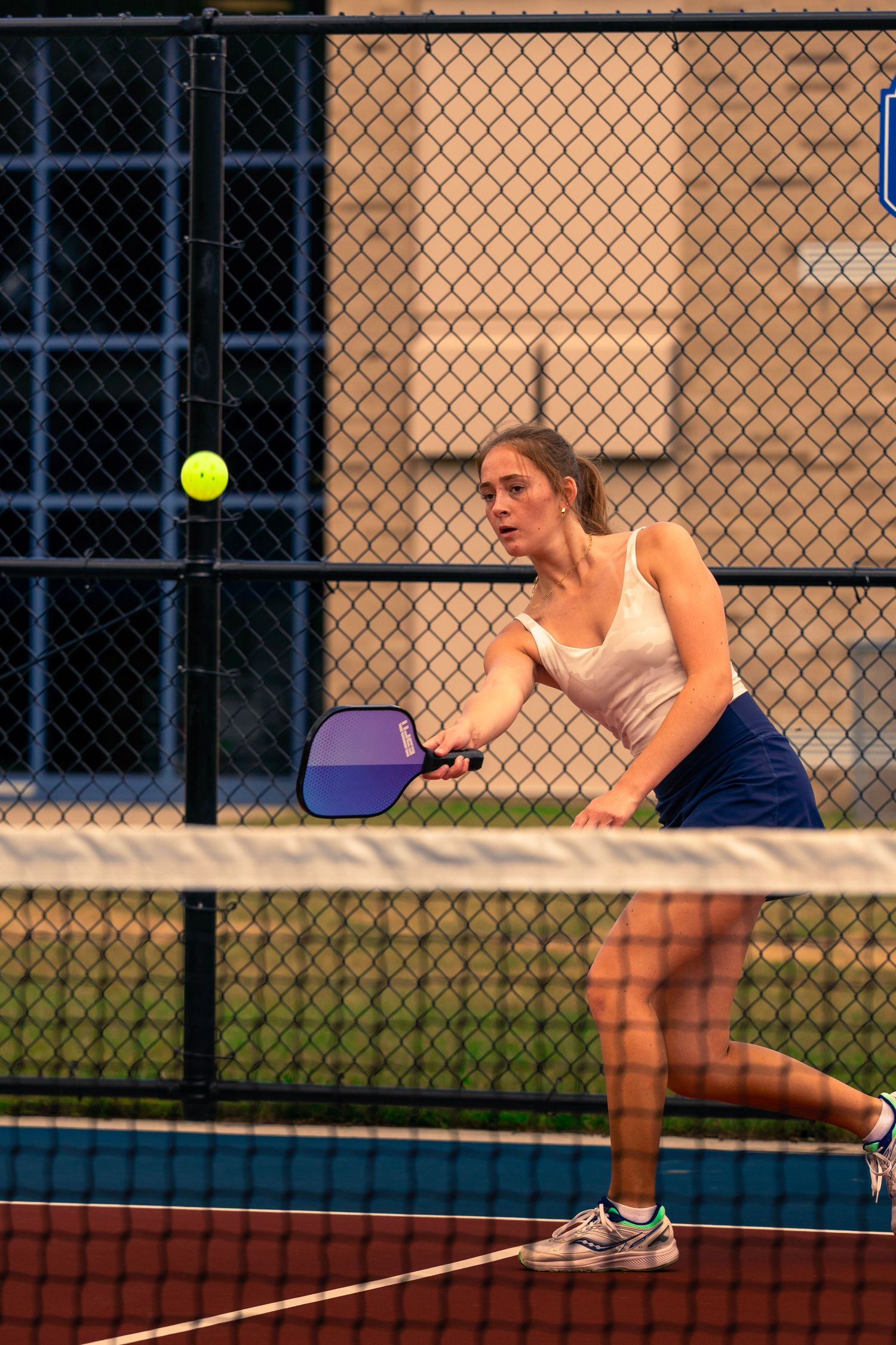 Tennis player stretches to hit a yellow ball during an intense match on an outdoor court.