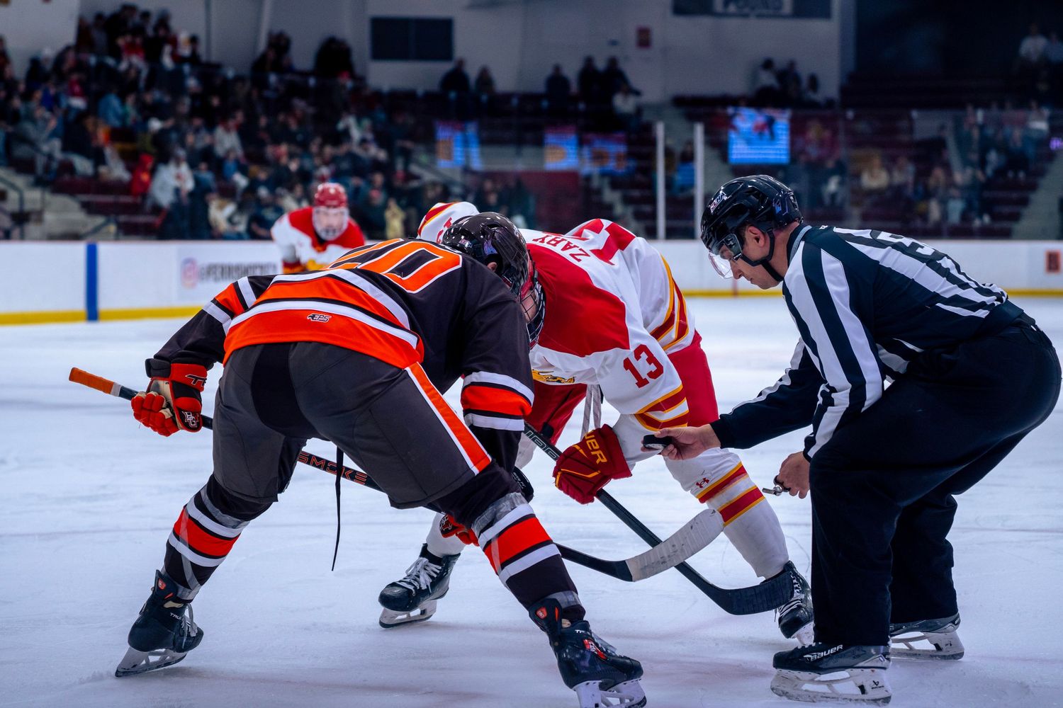 Hockey players face off at center ice during an intense NHL game between teams wearing red and dark jerseys.
