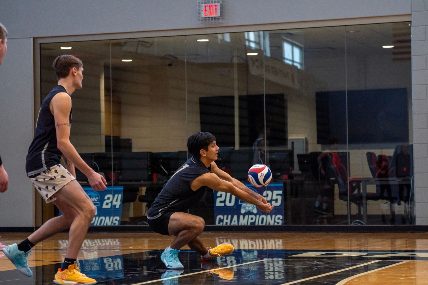 Two volleyball players dive for the ball during an intense match on an indoor court.