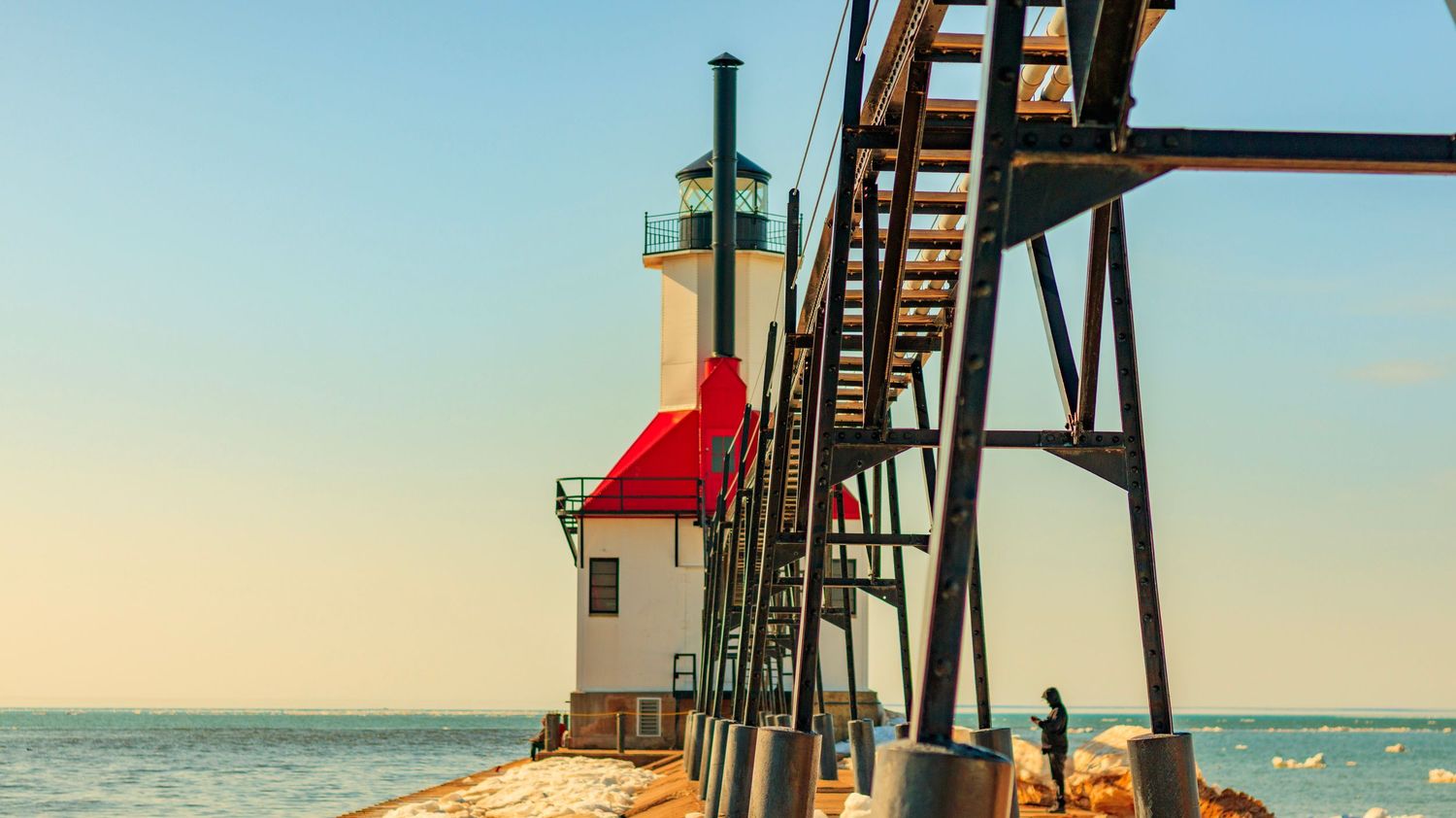 White lighthouse with red roof and metal catwalk pier extending over Lake Michigan.