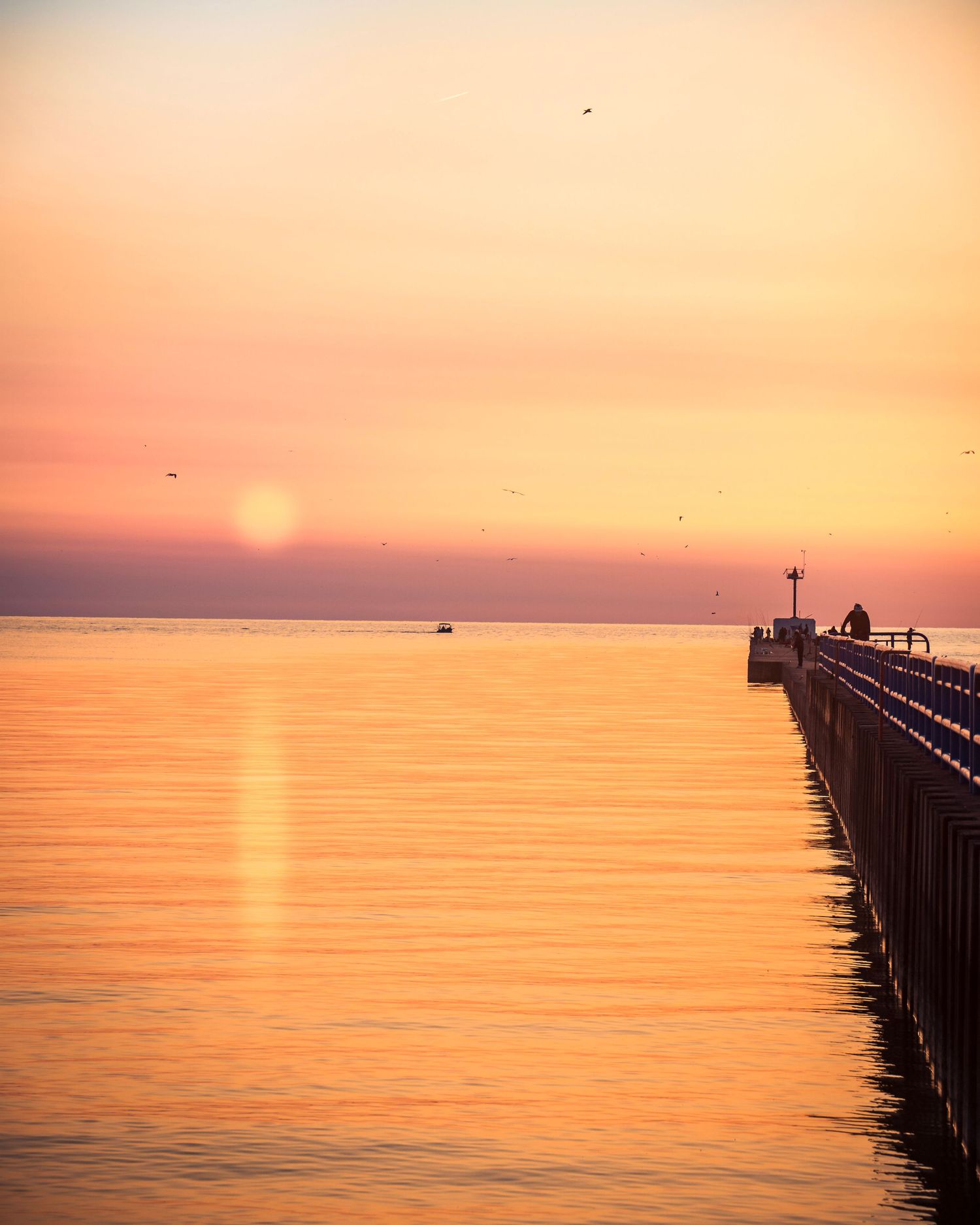 Long pier stretches into Lake Michigan during peaceful orange and pink sunset.