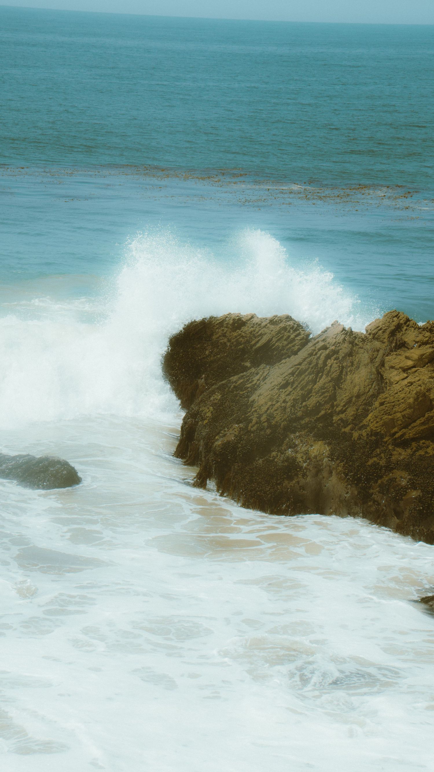 Powerful ocean waves crashing against dark rocky outcrops along the coastline.