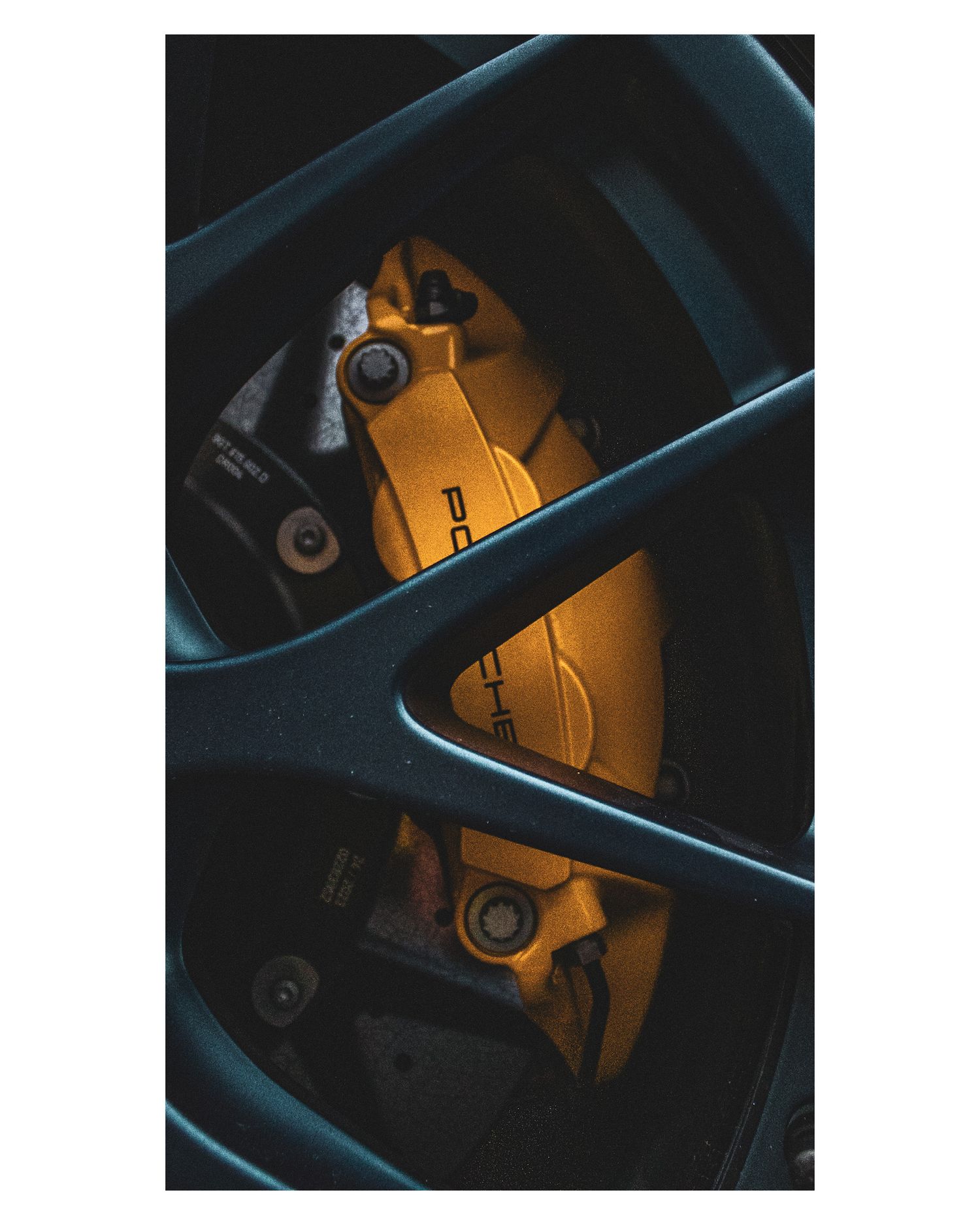 Close-up of yellow painted performance brake caliper visible through sports car wheel spokes.