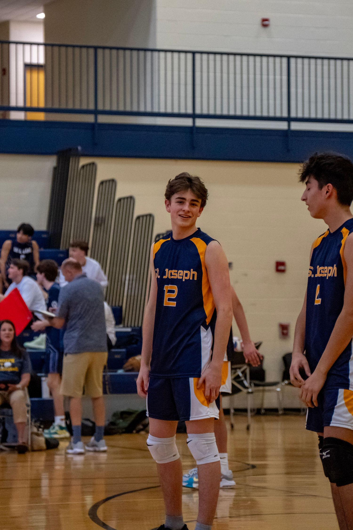 Players in St. Joseph navy and gold uniforms stand on the volleyball court.