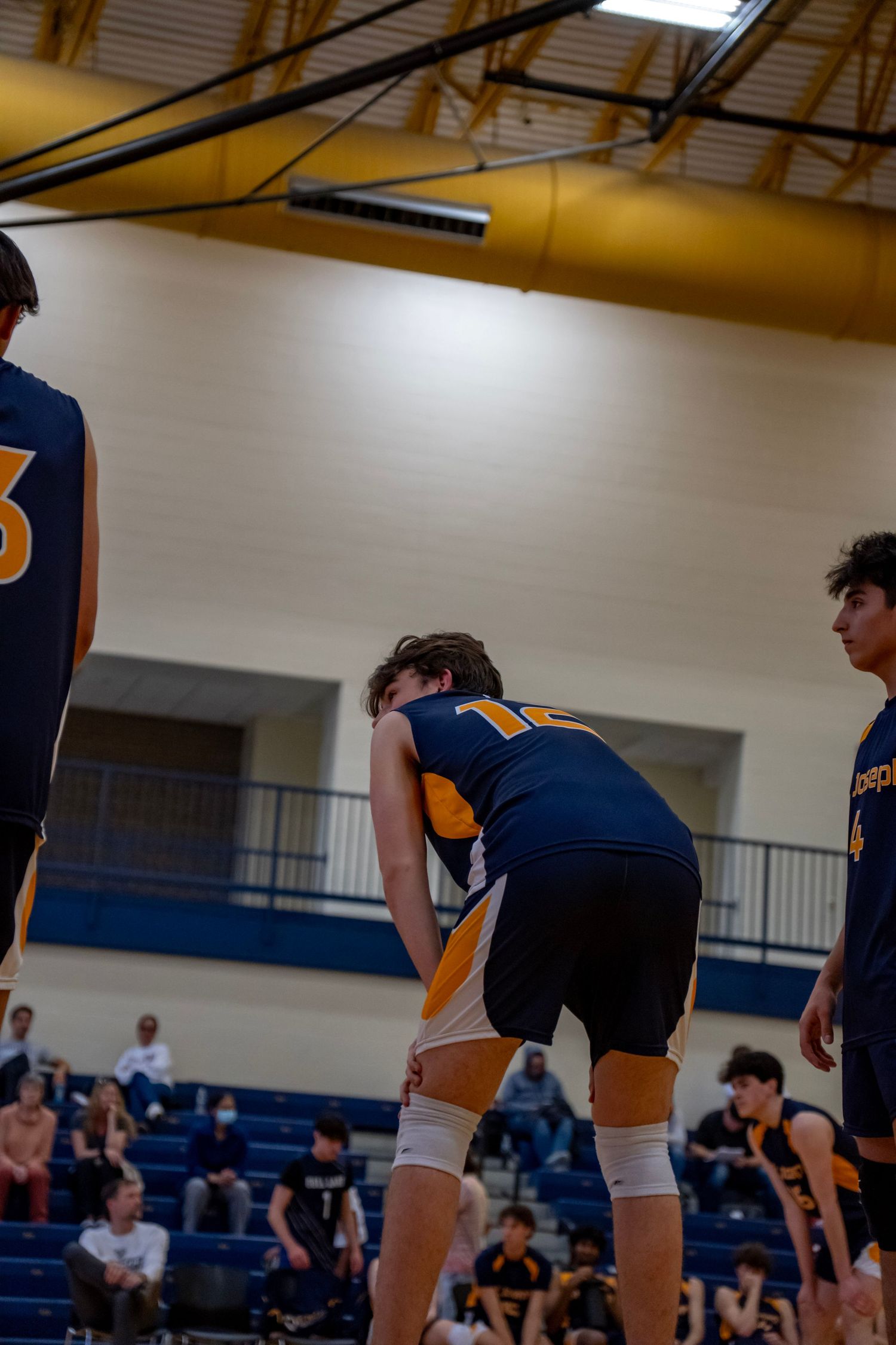 Players in navy uniforms position themselves on the volleyball court during a game.