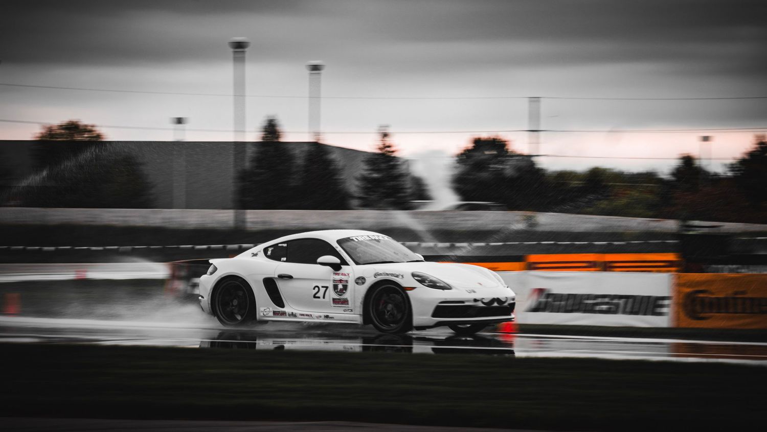 White sports car drifting on wet track in dramatic black and white.