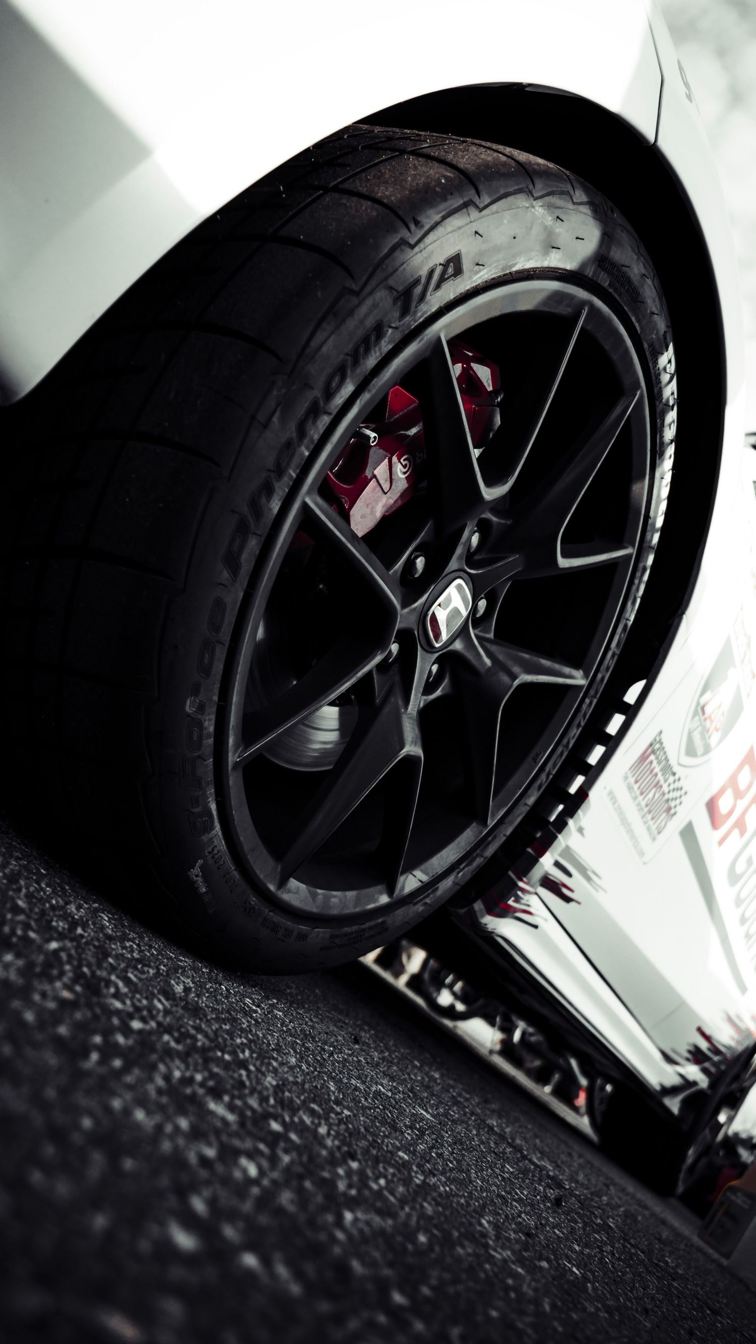 Detailed view of black alloy wheel with red brake caliper on race car.