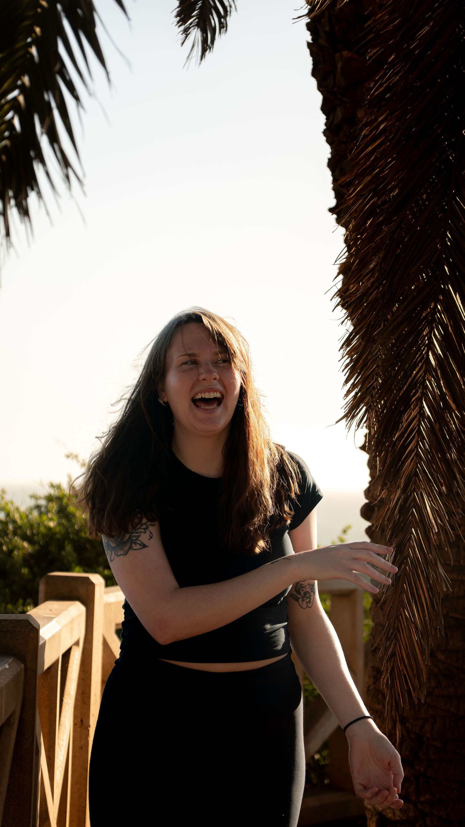 Candid laughing moment captured under palm trees with coastal backdrop.