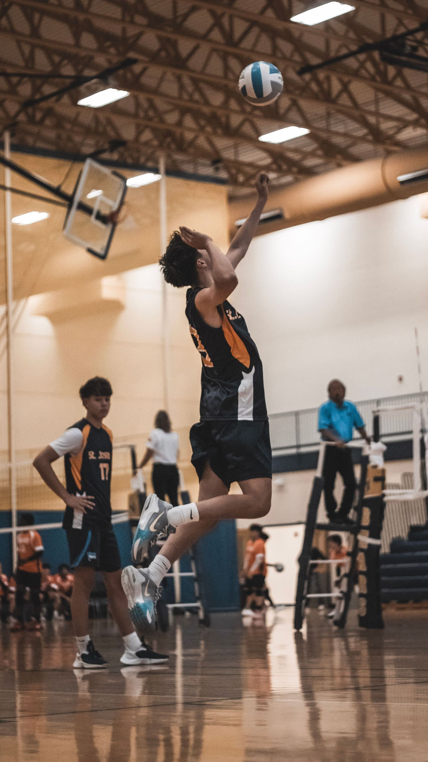 High school volleyball player leaps high to spike the ball during an indoor match.