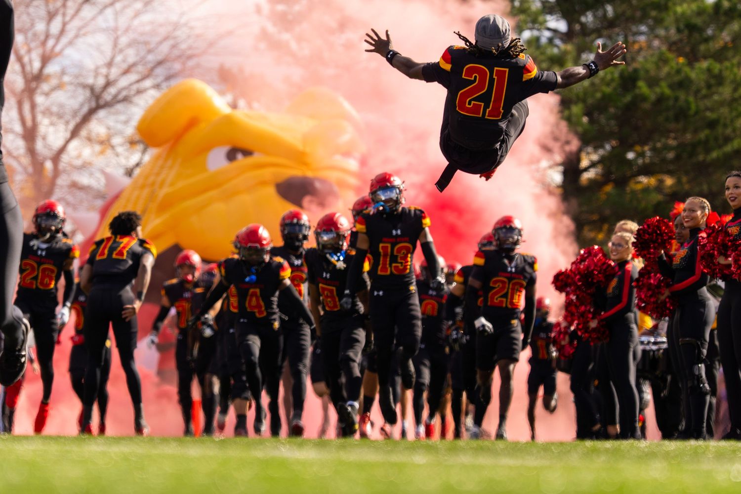 Soccer fans celebrate with red smoke flares and flags during an energetic outdoor sporting event.