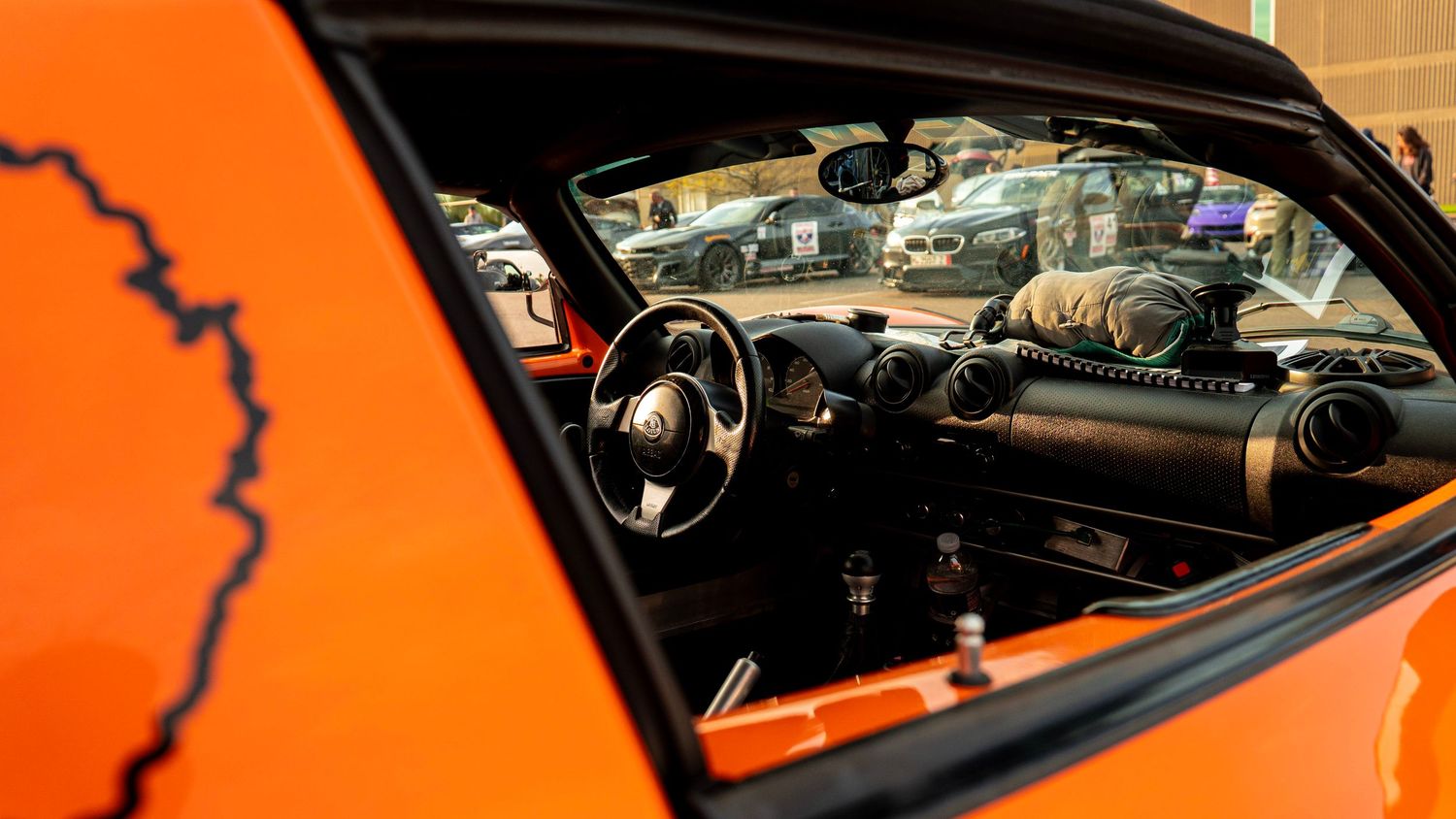 Side window view of orange Lotus car interior showing dashboard and controls.