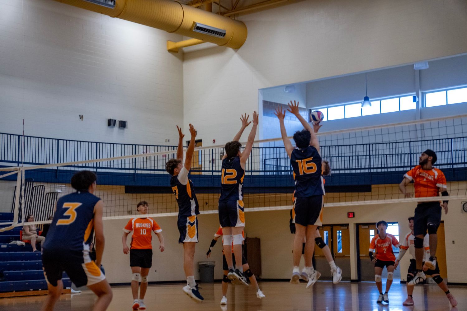 Indoor volleyball match shows players from both teams competing at the net.