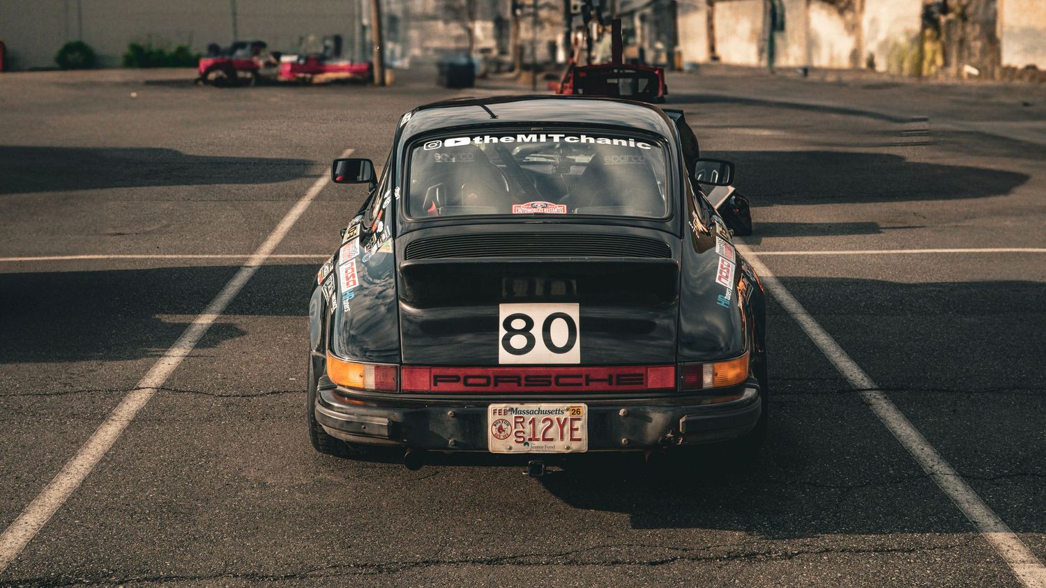 Rear three-quarter view of a black Porsche 911 race car with number 80 in parking space.