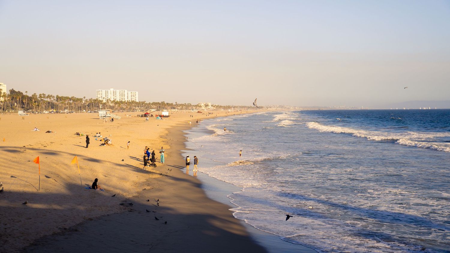 Wide panoramic view of a sandy beach at sunset with distant buildings along the coastline.