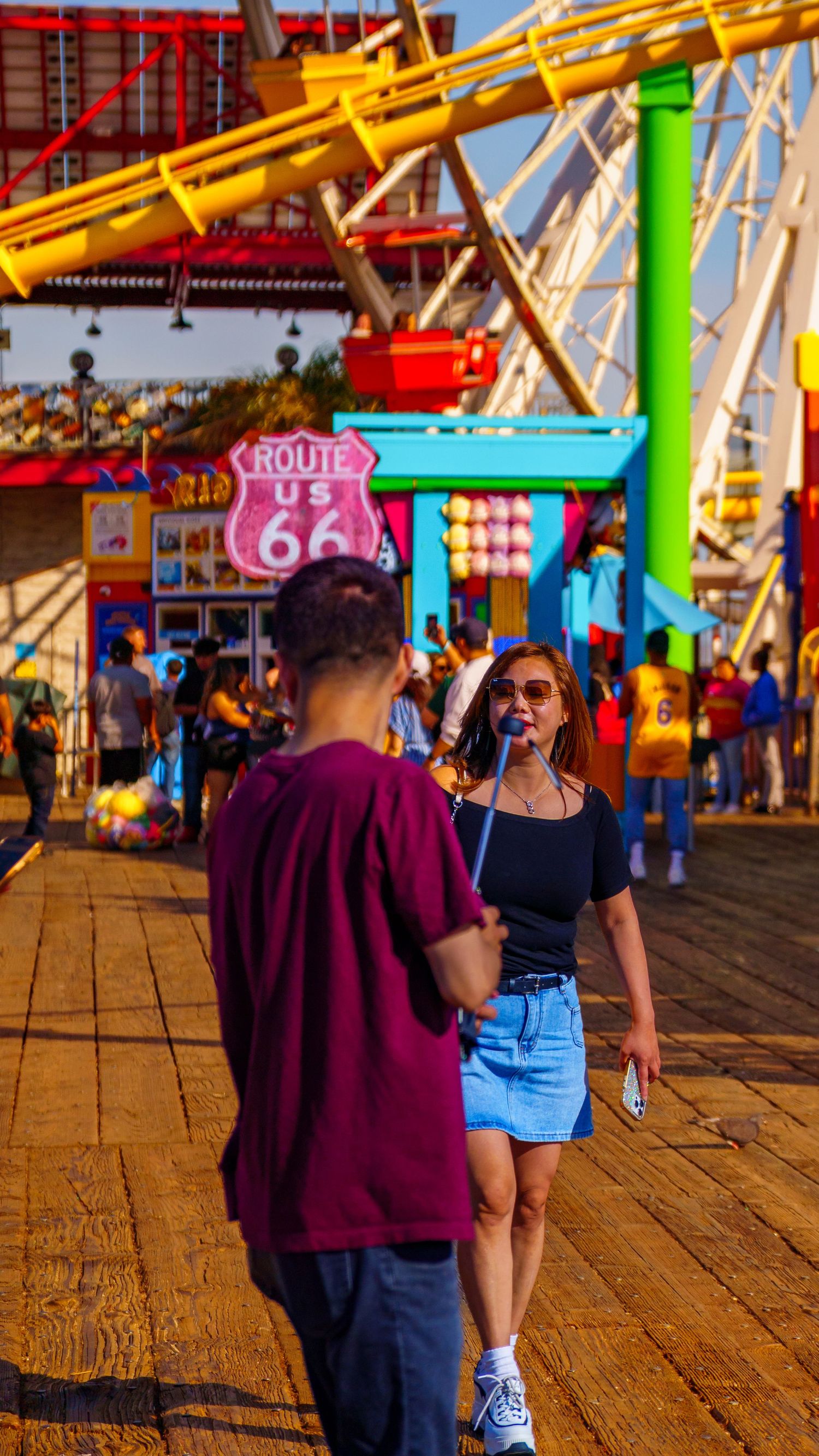 People walking along a colorful boardwalk with bright yellow overhead structures at dusk.