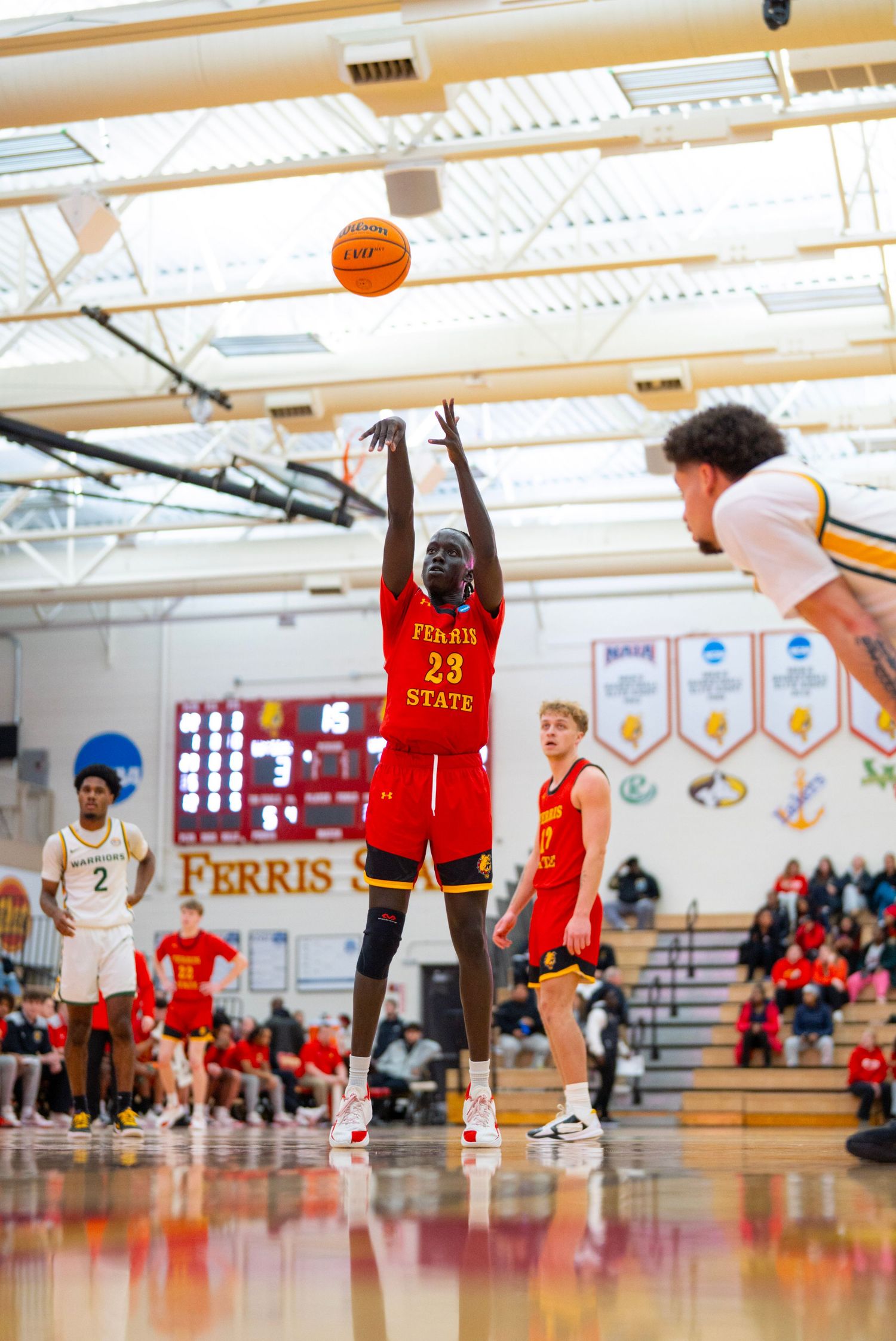 Basketball players compete in a high school gymnasium during a game between Ferris and an opposing team.