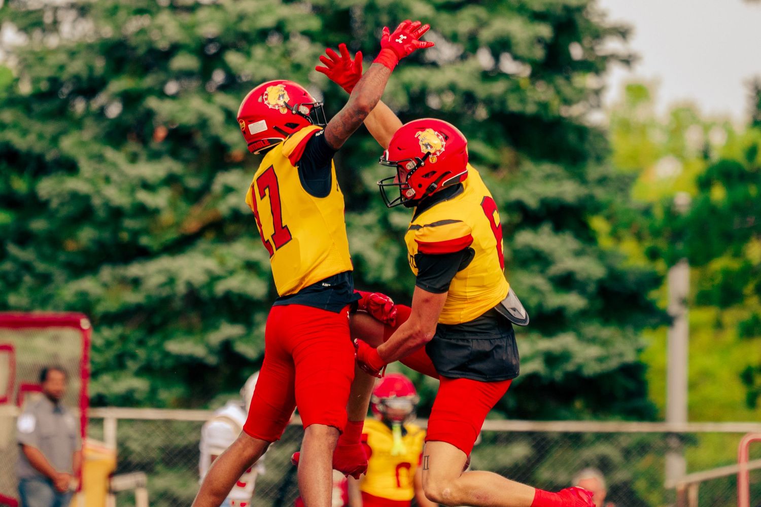 Football players in red and yellow uniforms compete during an intense game on a sunny field.