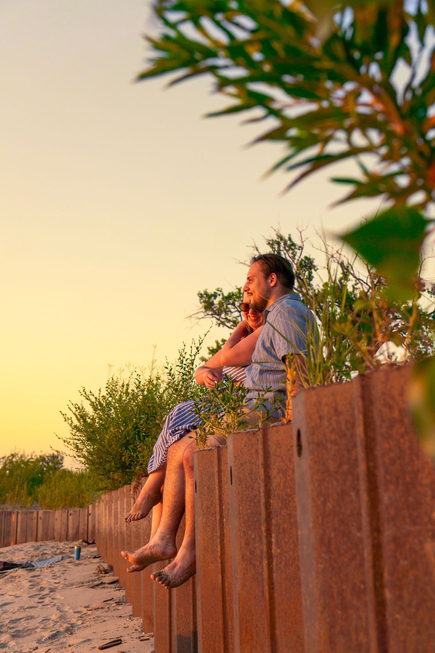 Two people sitting on a wooden beach boardwalk at sunset enjoying the peaceful coastal view.