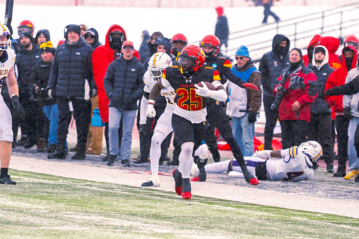 Football players and spectators gather on a snowy field during a cold winter game day.
