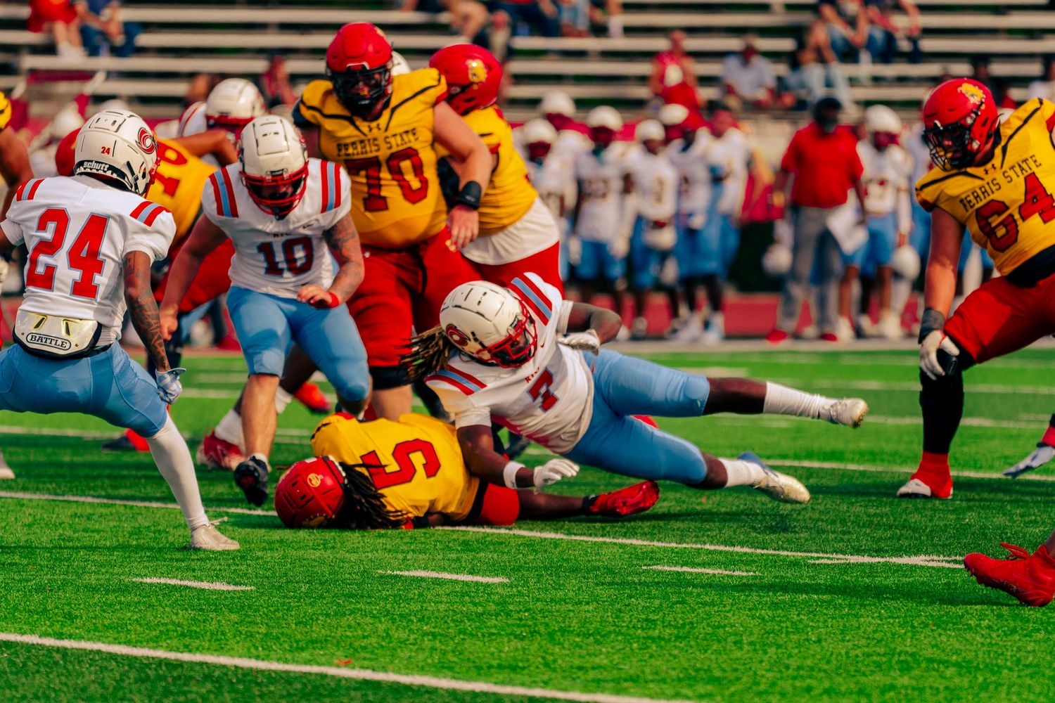 Football players in red and yellow uniforms collide during an intense play on the green turf field.