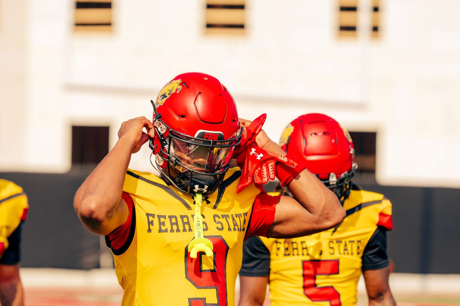 Football players in red helmets and yellow jerseys stand in formation during practice.