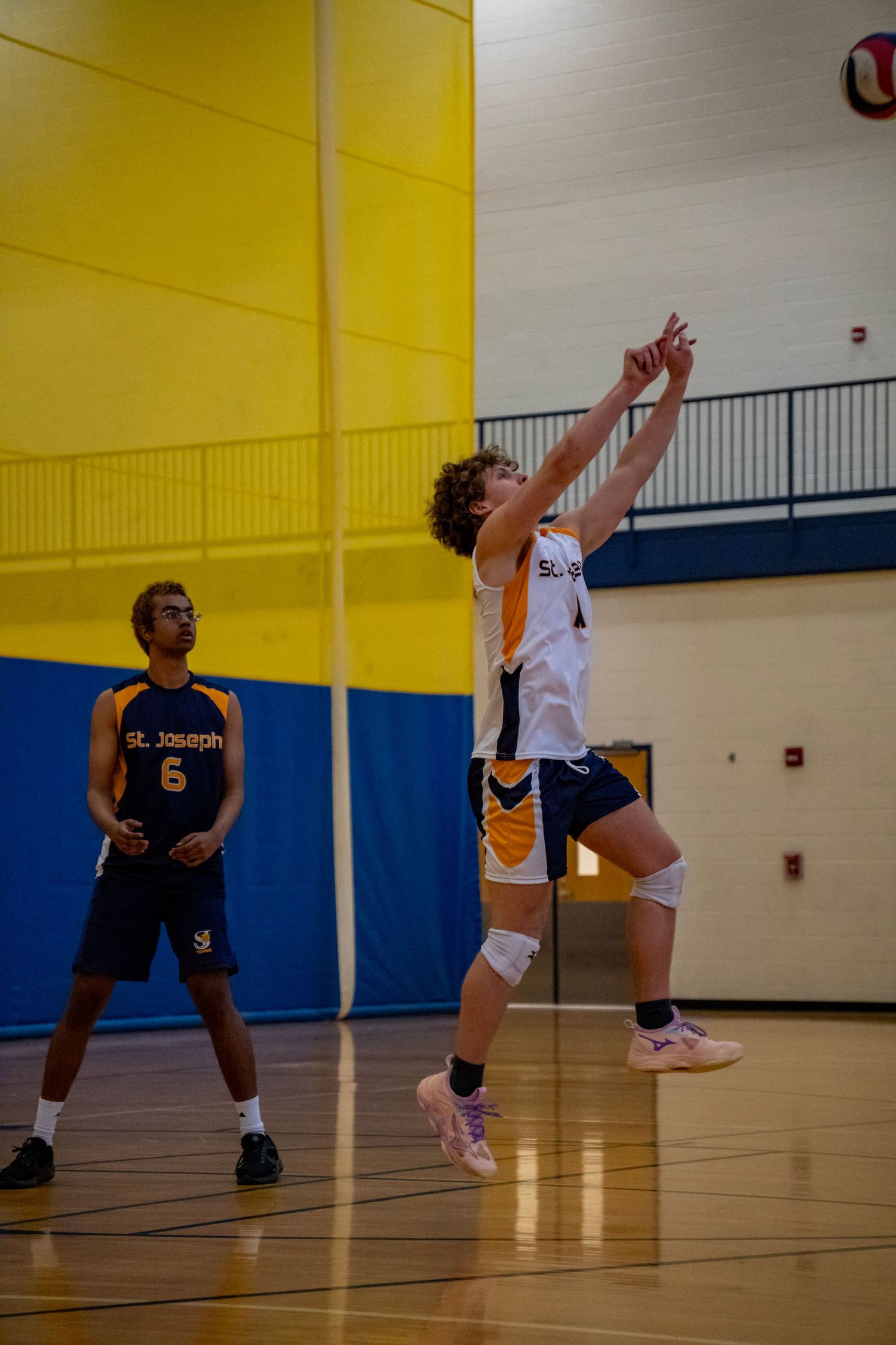 Player jumps to hit volleyball while opponent watches during competitive indoor match.