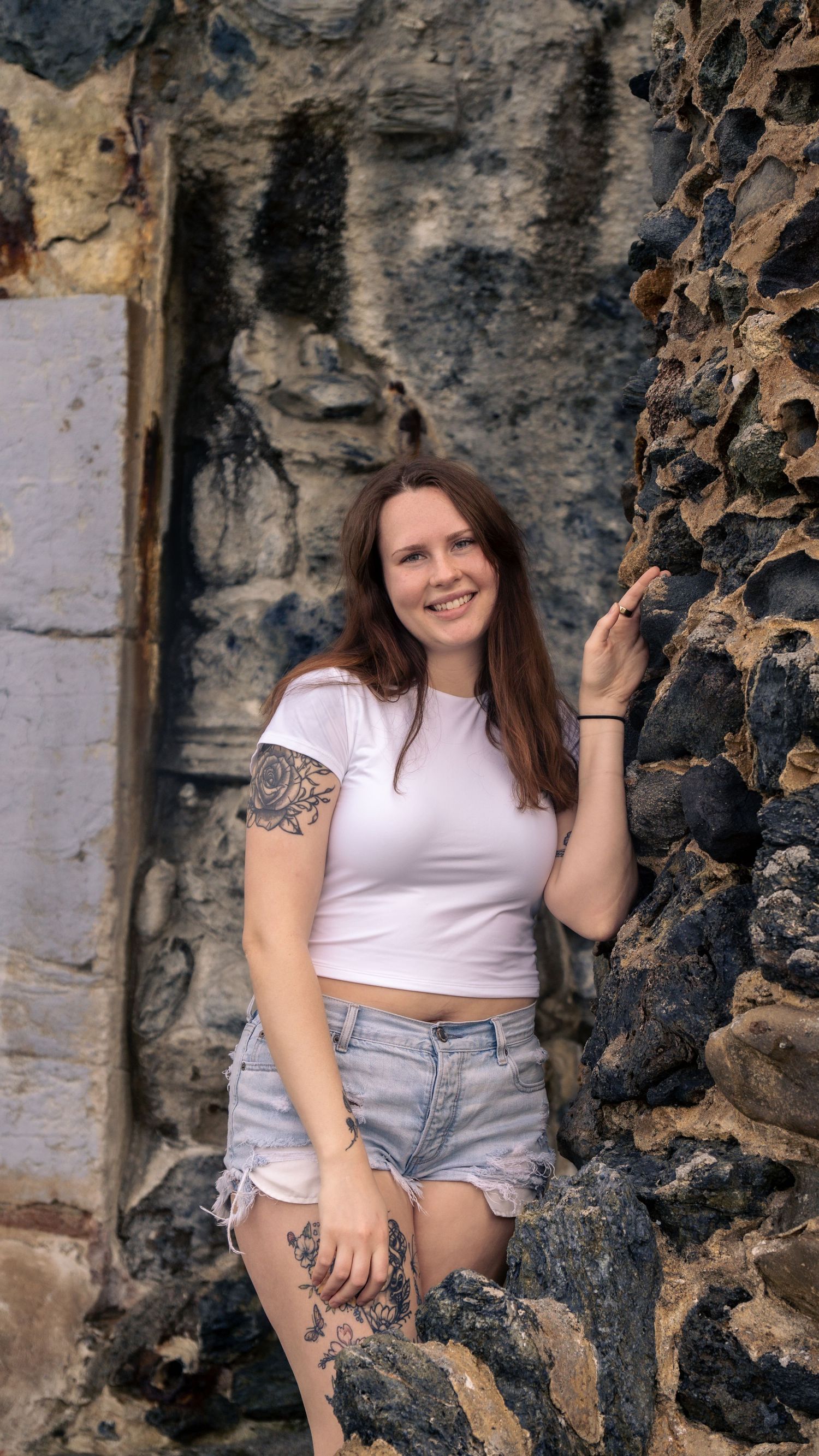 Fashion portrait against dark stone wall showing casual summer outfit and tattoo details.