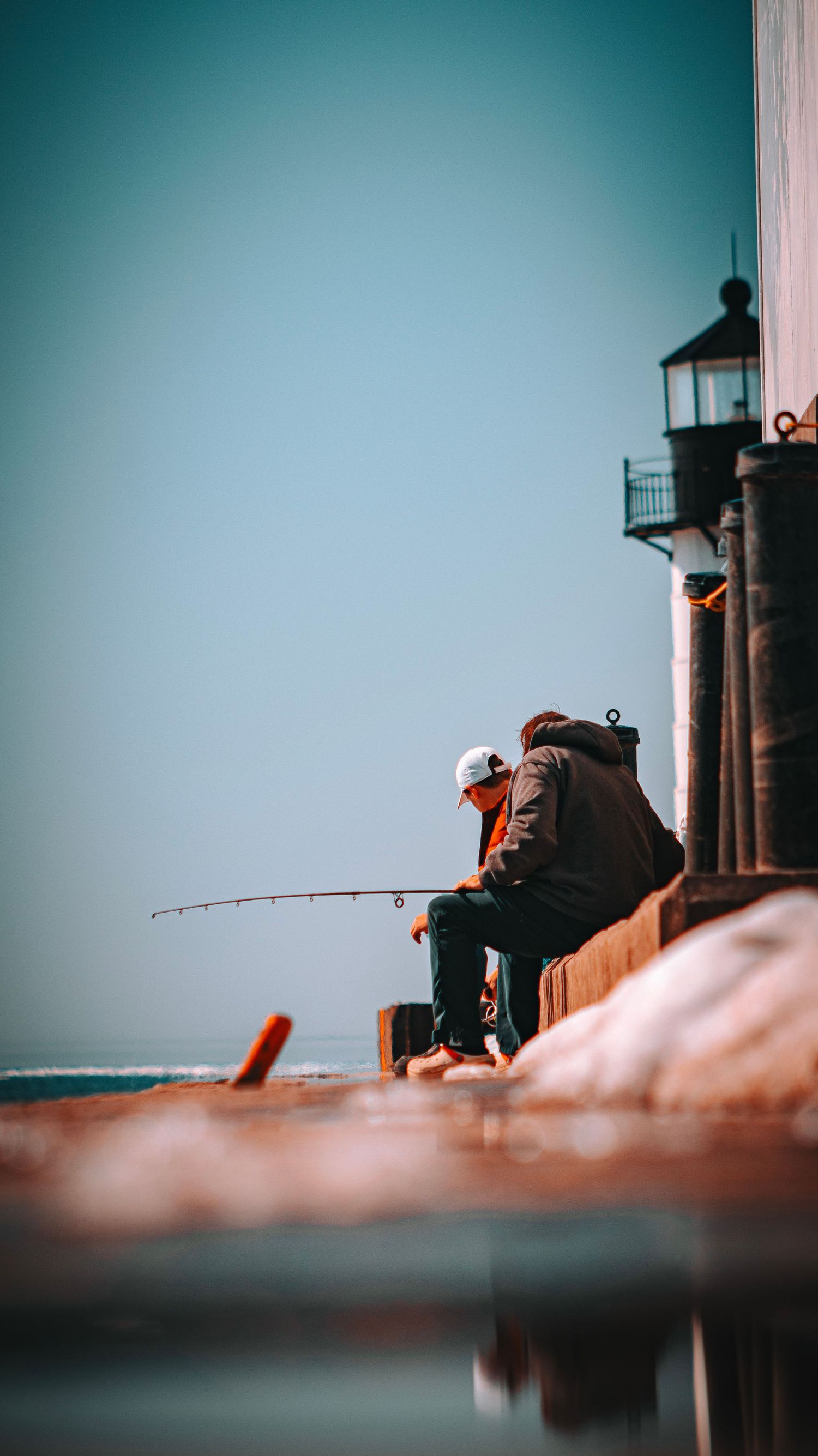 Silhouette of person fishing near lighthouse during golden hour.