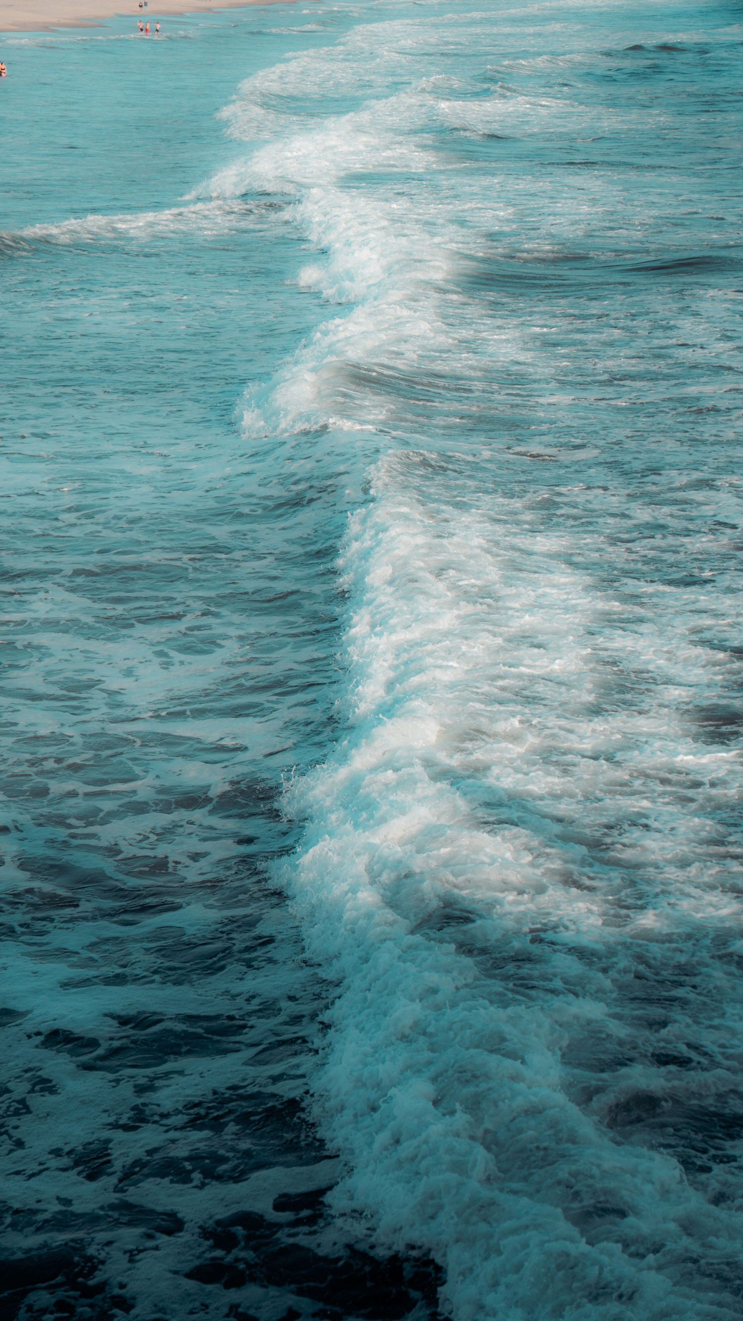 Turquoise ocean waves create a white wake pattern stretching across calm waters.
