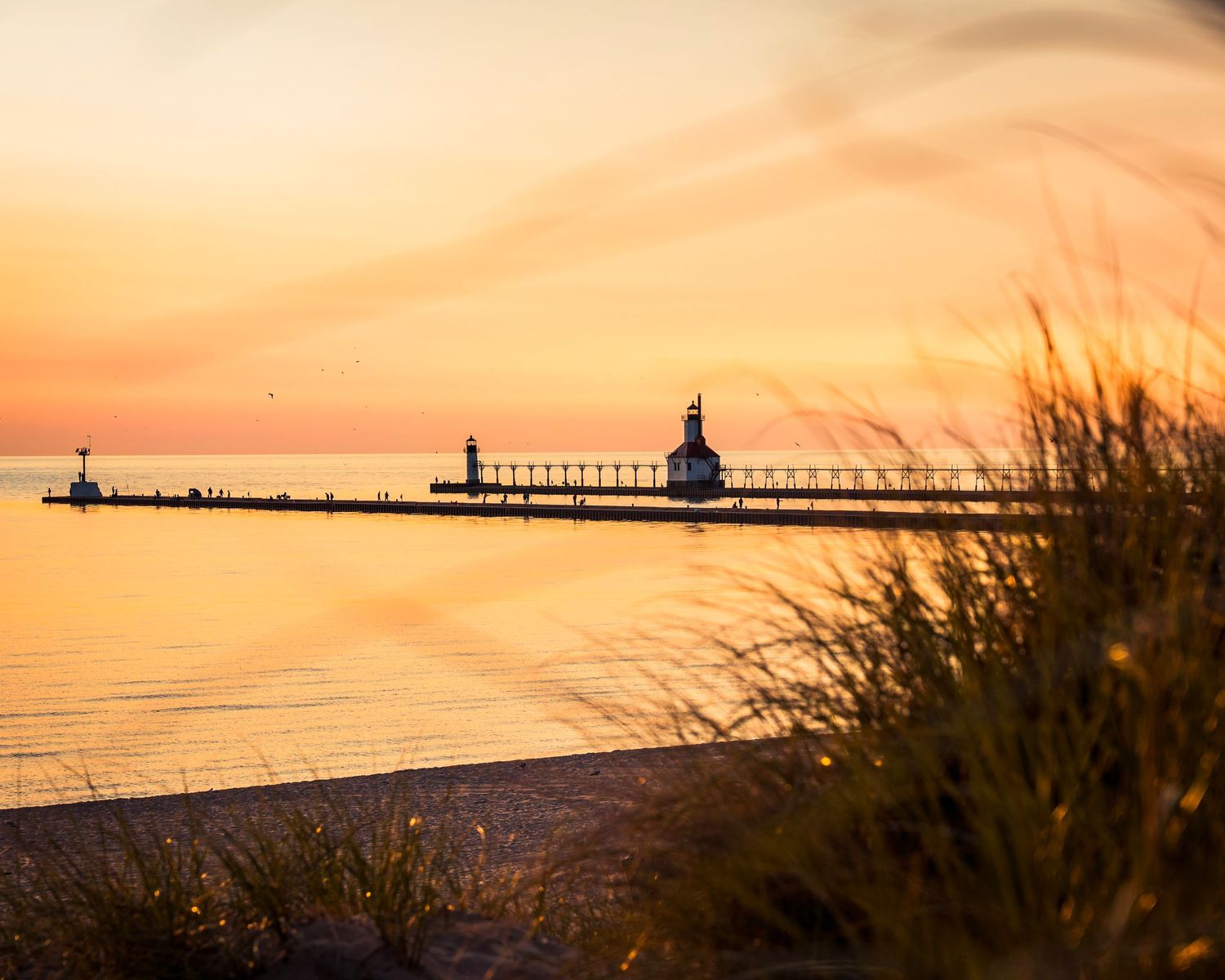 Lighthouse and pier casting long shadows during golden hour at a Lake Michigan beach.