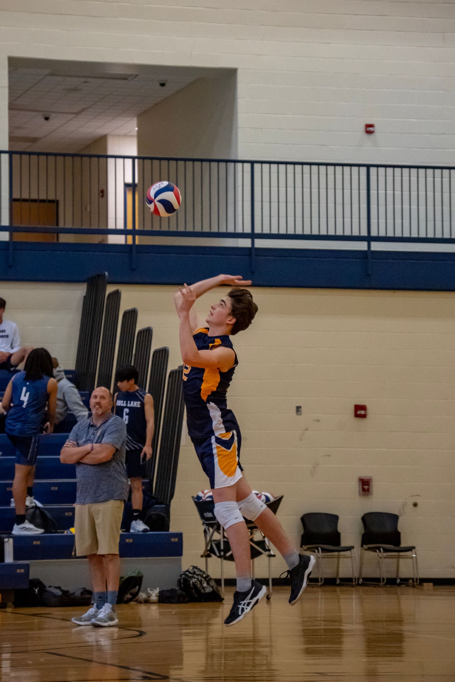 High school volleyball player in orange and navy jersey sets the ball during an indoor match.
