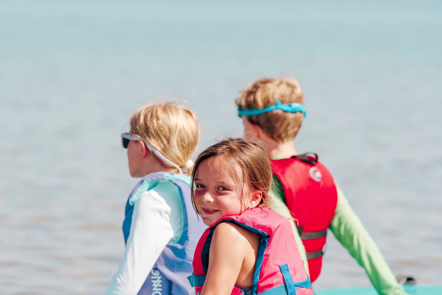 Children play and splash in shallow ocean water on a bright sunny day at the beach.
