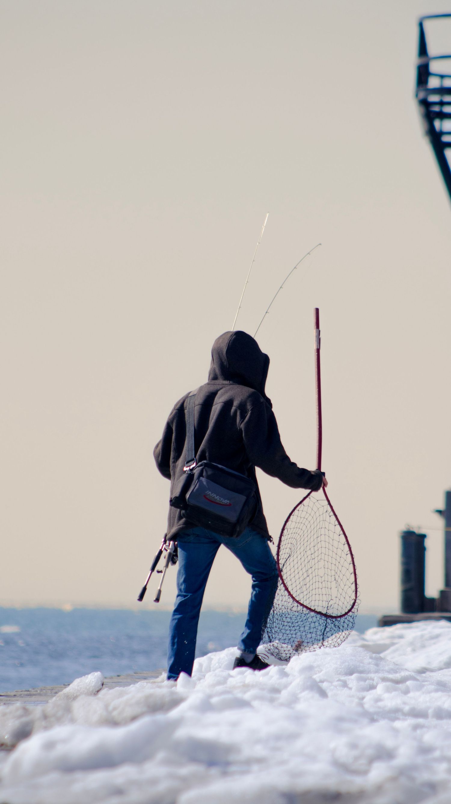 Winter fishing scene with person carrying net and rod on snowy pier.