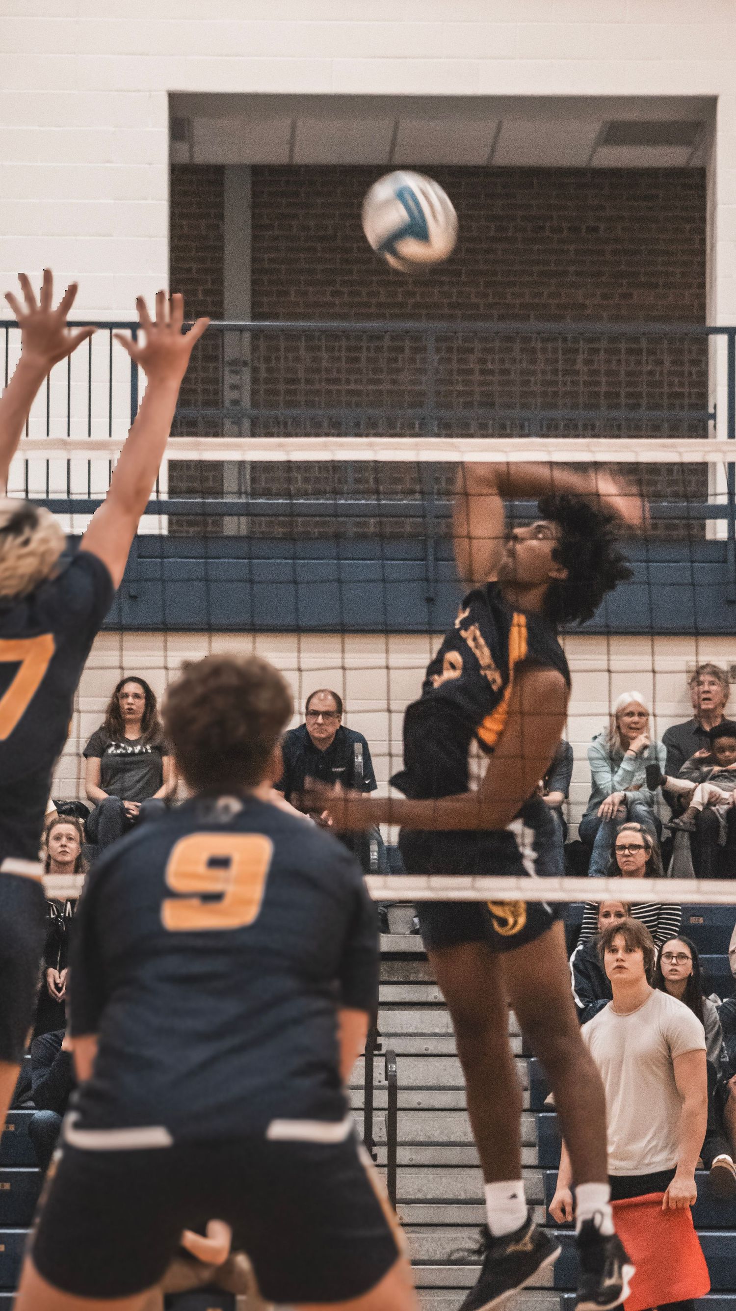 Two players jump at the volleyball net attempting to block a spike in an indoor gym.