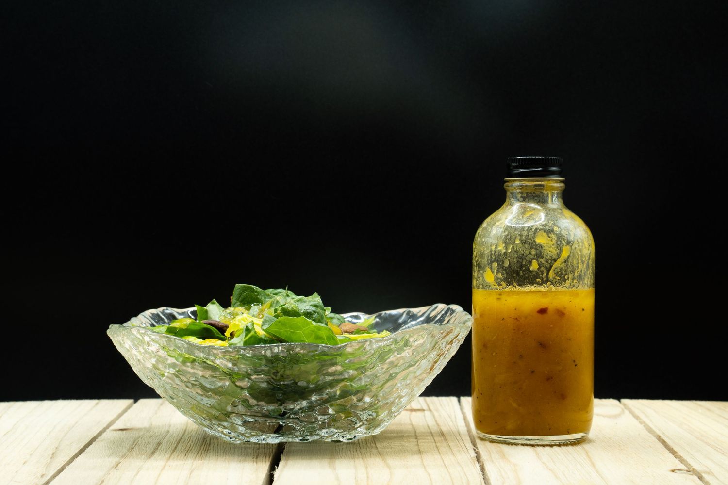 Fresh garden salad in crystal bowl with orange vinaigrette dressing on wooden surface.