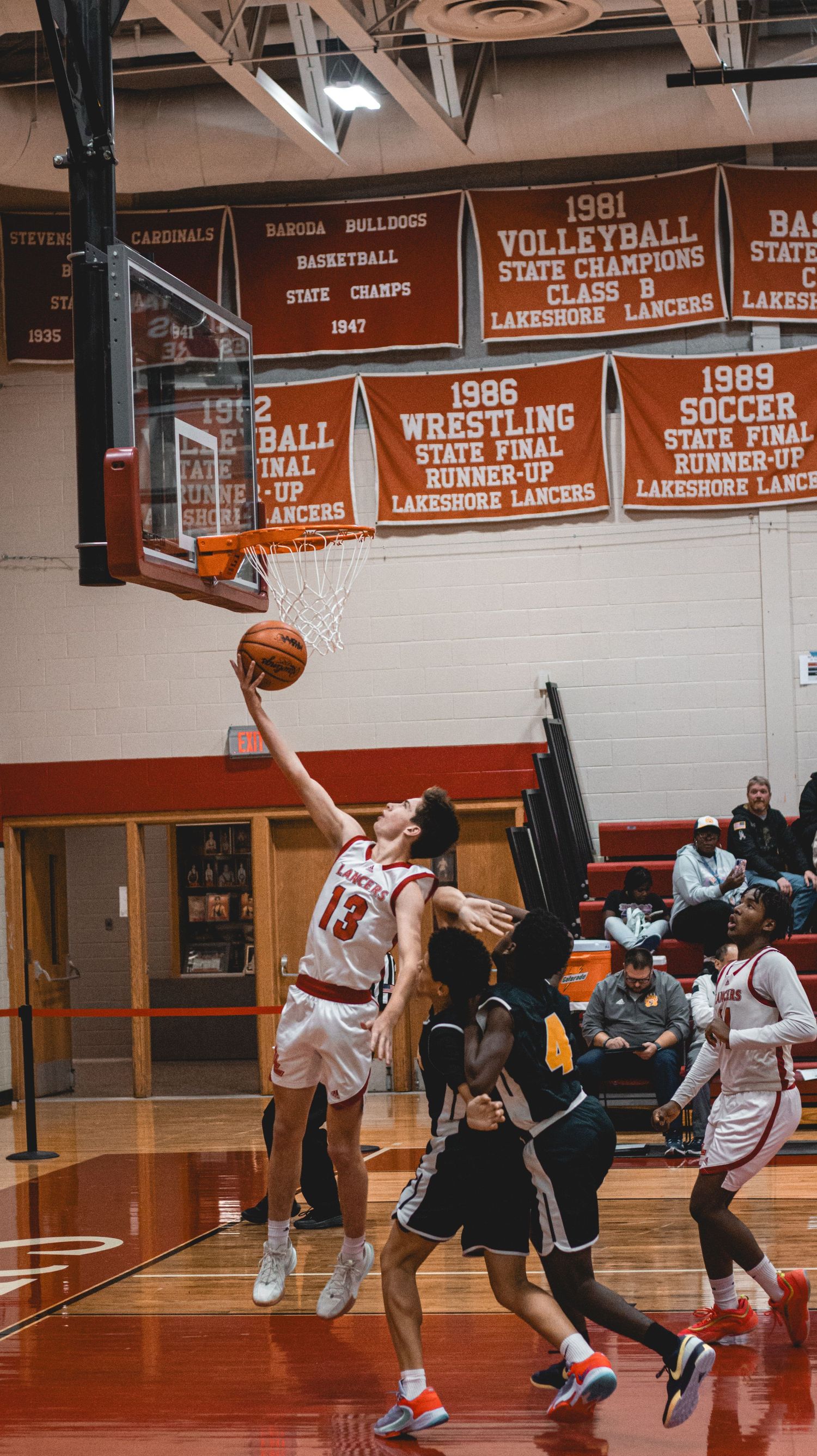 Player makes layup attempt during basketball game with championship banners visible above.