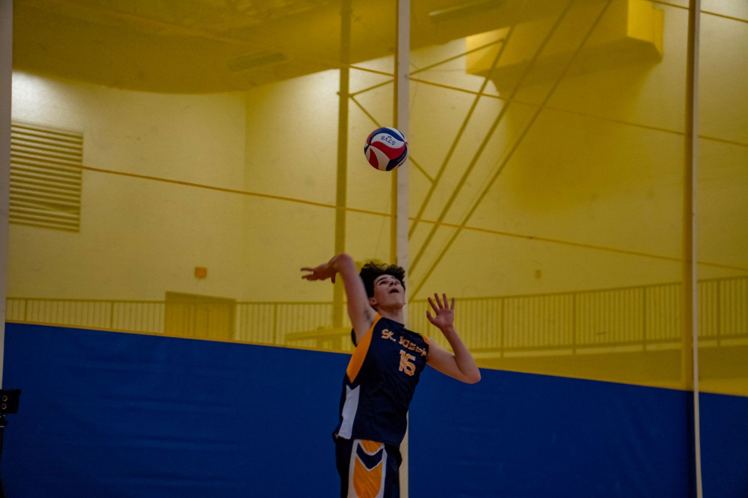 A volleyball player executes a powerful jump serve during an indoor game.